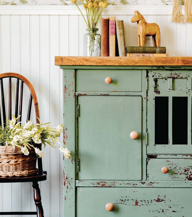 Charming vintage-style cabinet with distressed green paint, books, decorative wooden horse, and a basket of flowers for home décor.