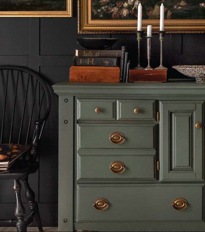 Elegant green dresser with gold hardware, candles, books, and black wall, showcasing modern home décor and premium paint finishes.