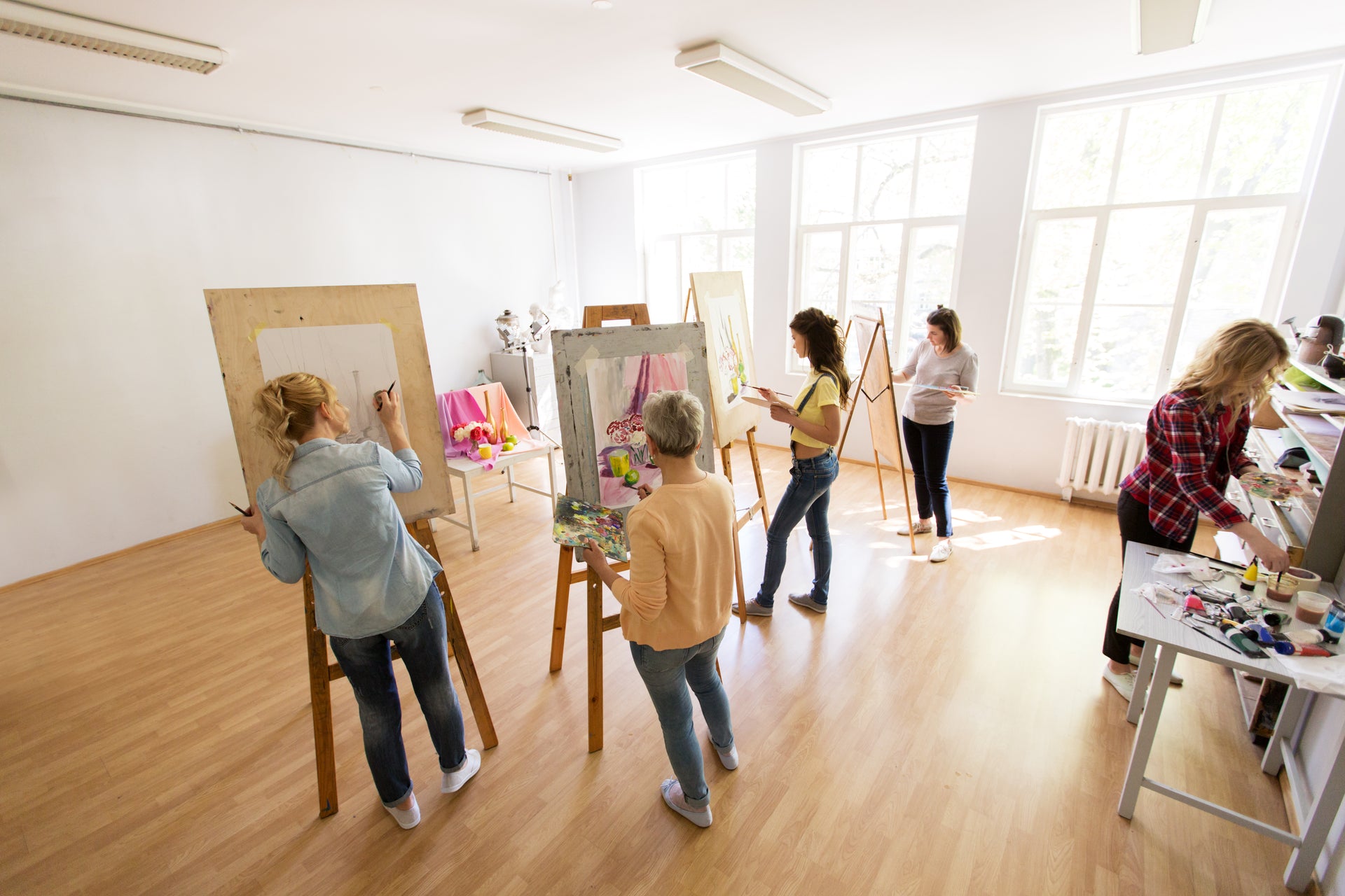 Art class participants using premium paints and painting tools to create DIY décor supplies on easels in a bright studio.
